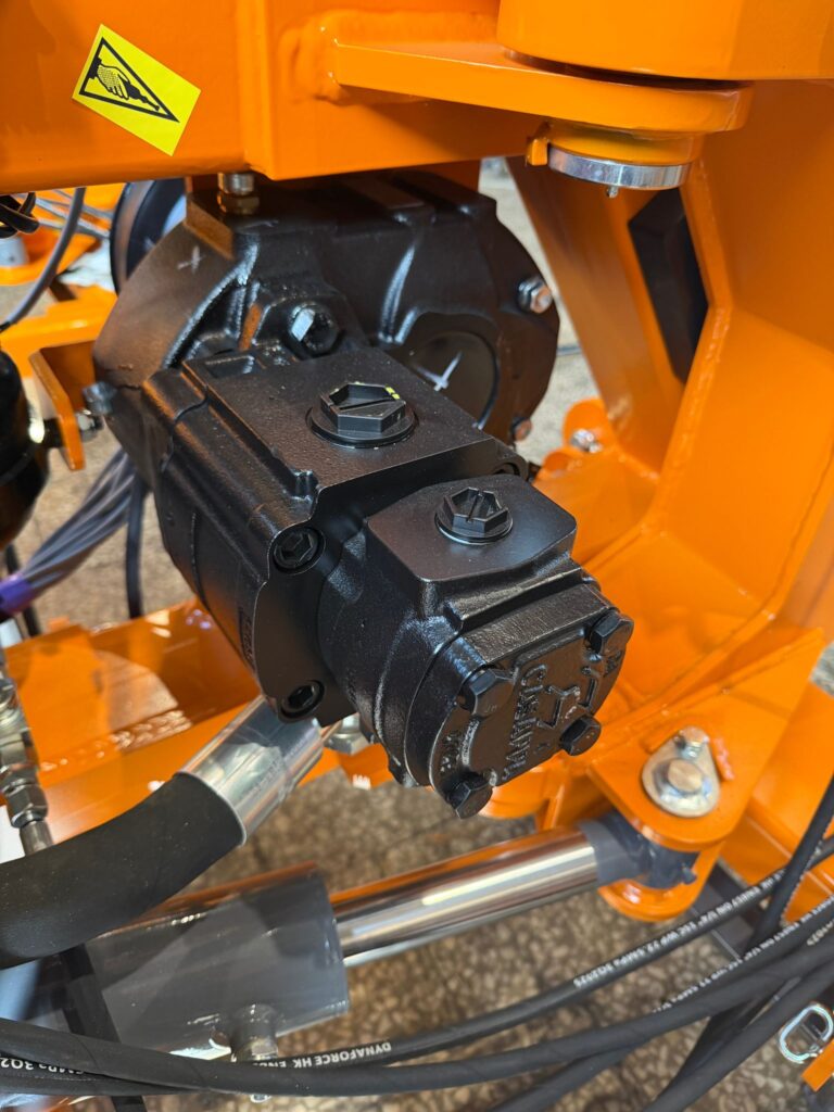 Pompa aluminiowa, żeliwna czy wysokociśnieniowa? Jaką hydraulikę wybrać do kosiarki wysięgnikowej W maszynach takich jak kosiarki wysięgnikowe oraz kosiarki bijakowe na koparki można spotkać trzy podstawowe koncepcje zasilania hydraulicznego. Pierwsza to układ aluminiowy, najczęściej obecny w rozwiązaniach budżetowych. Druga to układ żeliwny oparty na pompie zębatej i silniku zębatym. Trzecia to układ wysokociśnieniowy, zwykle z pompą tłokową. Literatura techniczna od lat pokazuje, że pompy zębate są cenione za prostą i zwartą konstrukcję, a pompy wielotłoczkowe są stosowane tam, gdzie potrzebna jest praca przy wyższych ciśnieniach. Na poziomie katalogu układ wysokociśnieniowy wygląda bardzo dobrze. Daje wysokie ciśnienie, dobrą sprawność i dużą gęstość mocy. Badania i opracowania dotyczące pomp osiowo tłokowych potwierdzają, że ich zaletami są wysoka sprawność, odporność na wysokie ciśnienia i szeroki zakres zastosowań w maszynach roboczych. Jednocześnie są to układy bardziej złożone i wrażliwsze na warunki pracy niż proste pompy zębate. Dlatego przy zakupie nie warto patrzeć wyłącznie na liczbę barów. W praktyce liczy się cały bilans: moc hydrauliczna, koszt układu, trwałość, czystość oleju, filtracja, dostępność serwisu i koszt regeneracji. To właśnie z tej perspektywy bardzo często najlepiej wypada układ żeliwny z pompą zębatą i silnikiem zębatym. Trzy podstawowe układy hydrauliczne stosowane w kosiarkach wysięgnikowych Układ aluminiowy To najtańsza grupa rozwiązań. Zwykle pracuje w zakresie około 180 do 190 bar i 90 do 100 l/min. Taki układ kusi ceną wejścia i może być wystarczający przy lżejszej pracy. Trzeba jednak uczciwie powiedzieć, że pod względem trwałości i zapasu do ciężkiej eksploatacji jest to najsłabsza z trzech opcji. Przy długiej pracy w poboczach, rowach, zakrzaczeniach i w trudnym terenie szybciej wychodzą jego ograniczenia. Układ żeliwny z pompą zębatą i silnikiem zębatym To rozwiązanie pośrednie cenowo, ale często najlepsze użytkowo. Typowy punkt pracy, który ma sens w cięższych kosiarkach wysięgnikowych, to około 230 bar i 120 l/min. Pompy zębate są szeroko stosowane właśnie dlatego, że mają prostą budowę, są zwarte konstrukcyjnie i dobrze wpisują się w układy, w których liczy się przewidywalność eksploatacji. Układ wysokociśnieniowy Tu najczęściej mówimy o pompach tłokowych i ciśnieniach rzędu około 320 bar przy przepływie około 80 l/min. Tego typu rozwiązania są technicznie uzasadnione tam, gdzie potrzebna jest wysoka sprawność i duża odporność na wysokie obciążenie ciśnieniowe. Materiały dydaktyczne i publikacje naukowe wskazują wprost, że pompy wielotłoczkowe pracują w układach o wyższych ciśnieniach, ponieważ zapewniają większą szczelność i dobre parametry robocze. Sama liczba barów nie rozstrzyga tematu W hydraulice o mocy nie decyduje samo ciśnienie. Zależność jest prosta: moc hydrauliczna jest iloczynem przepływu i ciśnienia. W materiałach dydaktycznych dla hydrauliki siłowej zapisuje się to jako P = Q · p, a po przeliczeniu dla bar i l/min otrzymujemy praktyczny wzór P [kW] = p [bar] × Q [l/min] / 600. Dla trzech porównywanych układów daje to: Układ aluminiowy 180 bar × 100 l/min = 30 kW 190 bar × 90 l/min = 28,5 kW Układ żeliwny zębaty 230 bar × 120 l/min = 46 kW Układ wysokociśnieniowy 320 bar × 80 l/min = 42,7 kW Wniosek jest prosty. Typowy układ żeliwny 230 bar i 120 l/min daje większą moc hydrauliczną niż typowy układ wysokociśnieniowy 320 bar i 80 l/min. To ważne z punktu widzenia klienta, bo pokazuje, że wyższe ciśnienie nie musi oznaczać mocniejszej maszyny. Trzeba oceniać cały układ, a nie tylko jeden parametr z folderu. Co mówi literatura techniczna i badania o pompach tłokowych Jeżeli spojrzeć na publikacje naukowe dotyczące pomp osiowo tłokowych, obraz jest dość spójny. To konstrukcje o wysokiej sprawności, dużej odporności na wysokie ciśnienia i wysokiej gęstości mocy. Badania publikowane w czasopismach technicznych pokazują też, że sprawność całkowita i objętościowa pomp osiowo tłokowych silnie zależy od ciśnienia, prędkości obrotowej, temperatury oleju i lepkości medium. Wzrost temperatury wejściowej i spadek lepkości pogarszają ich parametry pracy. Z praktycznego punktu widzenia oznacza to tyle, że pompa tłokowa jest rozwiązaniem dobrym, ale bardziej wymagającym. W maszynie pracującej ciężko i długo, poza samą sprawnością zaczyna liczyć się koszt utrzymania tej sprawności. Dlaczego układ żeliwny jest często najbardziej uzasadniony ekonomicznie Tu zaczyna się najważniejsza część dla użytkownika końcowego. W realnej eksploatacji kupuje się nie samą pompę, tylko cały układ i cały cykl życia maszyny. Pompy zębate są konstrukcyjnie prostsze i szeroko rozpowszechnione. To nie jest slogan handlowy, tylko cecha samej technologii, potwierdzana w materiałach dydaktycznych i pracach technicznych. Prostsza budowa zwykle oznacza łatwiejszy serwis, większą dostępność warsztatów i mniejszą zależność od bardzo precyzyjnej regeneracji. Z kolei pompy osiowo tłokowe wymagają dokładniejszej kontroli warunków pracy. Bosch Rexroth podkreśla, że nowoczesne komponenty hydrauliczne, zwłaszcza zawory proporcjonalne, serwozawory i pompy osiowo tłokowe, są bardzo wrażliwe na zanieczyszczenia cząstkami stałymi. Nawet pogorszenie klasy czystości o jeden stopień oznacza podwojenie koncentracji cząstek w oleju, co może prowadzić do wzrostu zużycia, pogorszenia pracy i awarii. To samo potwierdzają instrukcje techniczne producentów. Dla osiowych jednostek tłokowych Bosch Rexroth zaleca utrzymywanie klasy czystości oleju co najmniej 20/18/15 według ISO 4406, a przy wyższych temperaturach jeszcze lepszej. Wniosek praktyczny jest prosty. Im bardziej precyzyjny i wysilony układ, tym więcej kosztuje jego poprawna eksploatacja. Właśnie dlatego w praktyce serwisowej systemy wysokociśnieniowe są zwykle droższe nie tylko przy zakupie, ale też w przewodach, złączach, filtracji, regeneracji i postojach. Dokładna różnica cen zależy od producenta, klasy komponentów i konfiguracji maszyny, ale kierunek ekonomiczny jest jednoznaczny: wysoka sprawność kosztuje więcej. Wysokie ciśnienie ma sens, ale nie zawsze przy samej kosiarce Układ o większej mocy ma sens wtedy, gdy maszyna nie służy wyłącznie do lekkiego koszenia trawy. Przy odmulaniu rowów, czyszczeniu poboczy, pracy w gęstych zaroślach czy mulczowaniu grubszych gałęzi większa moc na rotorze daje realną przewagę. Maszyna łatwiej utrzymuje obroty, mniej się dławi i lepiej radzi sobie z cięższym materiałem. To oznacza, że układ wysokiej mocy ma uzasadnienie nie tylko przy klasycznych kosiarkach wysięgnikowych, ale też wtedy, gdy osprzęt ma wykonywać cięższe prace terenowe i ziemne. W praktyce dotyczy to również maszyn takich jak kosiarki bijakowe na koparki, gdzie osprzęt pracuje na istniejącej hydraulice nośnika. Kiedy układ wysokociśnieniowy naprawdę ma sens Tu odpowiedź jest dość prosta. Układ wysokociśnieniowy ma największy sens wtedy, gdy nośnik już posiada takie zasilanie. Dobrym przykładem są koparki i inne maszyny robocze, gdzie hydraulika wysokiego ciśnienia jest już dostępna. W takiej sytuacji zastosowanie silnika wysokociśnieniowego do osprzętu jest logiczne, bo można wykorzystać gotową pompę i gotowy układ. To właśnie w takim scenariuszu kosiarki bijakowe na koparki mogą pracować na hydraulice wysokociśnieniowej z realnym uzasadnieniem. Nie buduje się wtedy osobnego zasilania od zera, tylko korzysta z tego, co maszyna bazowa już ma. Jeżeli jednak klient dopiero wybiera cały układ do kosiarki wysięgnikowej, sytuacja wygląda inaczej. Wtedy wejście w system wysokociśnieniowy jest często wejściem w większe koszty bez proporcjonalnej korzyści użytkowej. Przy świadomym doborze od podstaw bardziej racjonalnym wyborem bywa żeliwna pompa zębata i żeliwny silnik zębaty. Co realnie zyskuje klient przy układzie żeliwnym 230 bar i 120 l/min Najpierw dostaje 46 kW mocy hydraulicznej, czyli poziom w pełni wystarczający do ciężkiej pracy w wielu zastosowaniach komunalnych, drogowych i melioracyjnych. To moc większa niż w typowym zestawie 320 bar i 80 l/min. Po drugie dostaje układ, który nie pracuje na skrajnie wysokim ciśnieniu, więc cały osprzęt hydrauliczny jest mniej obciążony. W praktyce przekłada się to na niższy koszt całego systemu. Po trzecie dostaje rozwiązanie prostsze serwisowo. W przypadku pomp zębatych łatwiej o dostęp do części, napraw i warsztatów. W przypadku pomp tłokowych znaczenie ma już nie tylko sama część, ale także bardzo wysoka jakość regeneracji i kultura serwisowa układu. Wnioski praktyczne Jeżeli najważniejsza jest najniższa cena wejścia, układ aluminiowy może być rozwiązaniem wystarczającym, ale trzeba zaakceptować jego mniejszą trwałość. Jeżeli nośnik ma już hydraulikę wysokiego ciśnienia, a osprzęt ma pracować ciężko i wielozadaniowo, układ wysokociśnieniowy może mieć sens. Jeżeli jednak wybór dotyczy budowy układu od zera, a celem jest rozsądny koszt zakupu, dobra moc, trwałość i przewidywalność eksploatacji, to w wielu przypadkach najbardziej uzasadniony pozostaje układ żeliwny z pompą zębatą i silnikiem zębatym, pracujący w okolicach 230 bar i 120 l/min. To nie jest wybór najbardziej efektowny na papierze. To jest wybór najbardziej racjonalny w praktyce. FAQ Czy wyższe ciśnienie zawsze oznacza lepszą kosiarkę wysięgnikową? Nie. O mocy hydraulicznej decydują razem ciśnienie i przepływ. Dlatego układ 230 bar i 120 l/min może dawać większą moc niż układ 320 bar i 80 l/min. Kiedy warto wybrać pompę tłokową? Głównie wtedy, gdy nośnik ma już gotową hydraulikę wysokiego ciśnienia albo gdy osprzęt ma pracować w bardzo wymagających warunkach i potrzebna jest wysoka sprawność przy dużym ciśnieniu. Dlaczego pompy tłokowe są bardziej wymagające? Ponieważ są precyzyjne, pracują przy wysokich ciśnieniach i są bardziej wrażliwe na czystość oleju oraz jakość filtracji. Producenci podają dla nich konkretne wymagania czystości oleju według ISO 4406. Czy kosiarki bijakowe na koparki powinny mieć osobny układ hydrauliczny? Nie zawsze. Jeżeli koparka ma już odpowiednią hydraulikę wysokiego ciśnienia, zwykle sensowniejsze jest wykorzystanie istniejącego zasilania niż budowa oddzielnego układu. Źródła i literatura Materiały dydaktyczne z hydrauliki siłowej dotyczące pomp zębatych i wielotłoczkowych. Bosch Rexroth, wymagania dotyczące czystości oleju i wrażliwości pomp osiowo tłokowych na zanieczyszczenia. Publikacje naukowe o pompach osiowo tłokowych i ich sprawności. Rozprawa techniczna dotycząca pomp zębatych i ich konstrukcji. Fraza główna: kosiarki wysięgnikowe Frazy dodatkowe: kosiarki bijakowe na koparki, hydraulika w kosiarce wysięgnikowej, pompa zębata do kosiarki wysięgnikowej, pompa tłokowa do kosiarki, układ wysokociśnieniowy w kosiarce