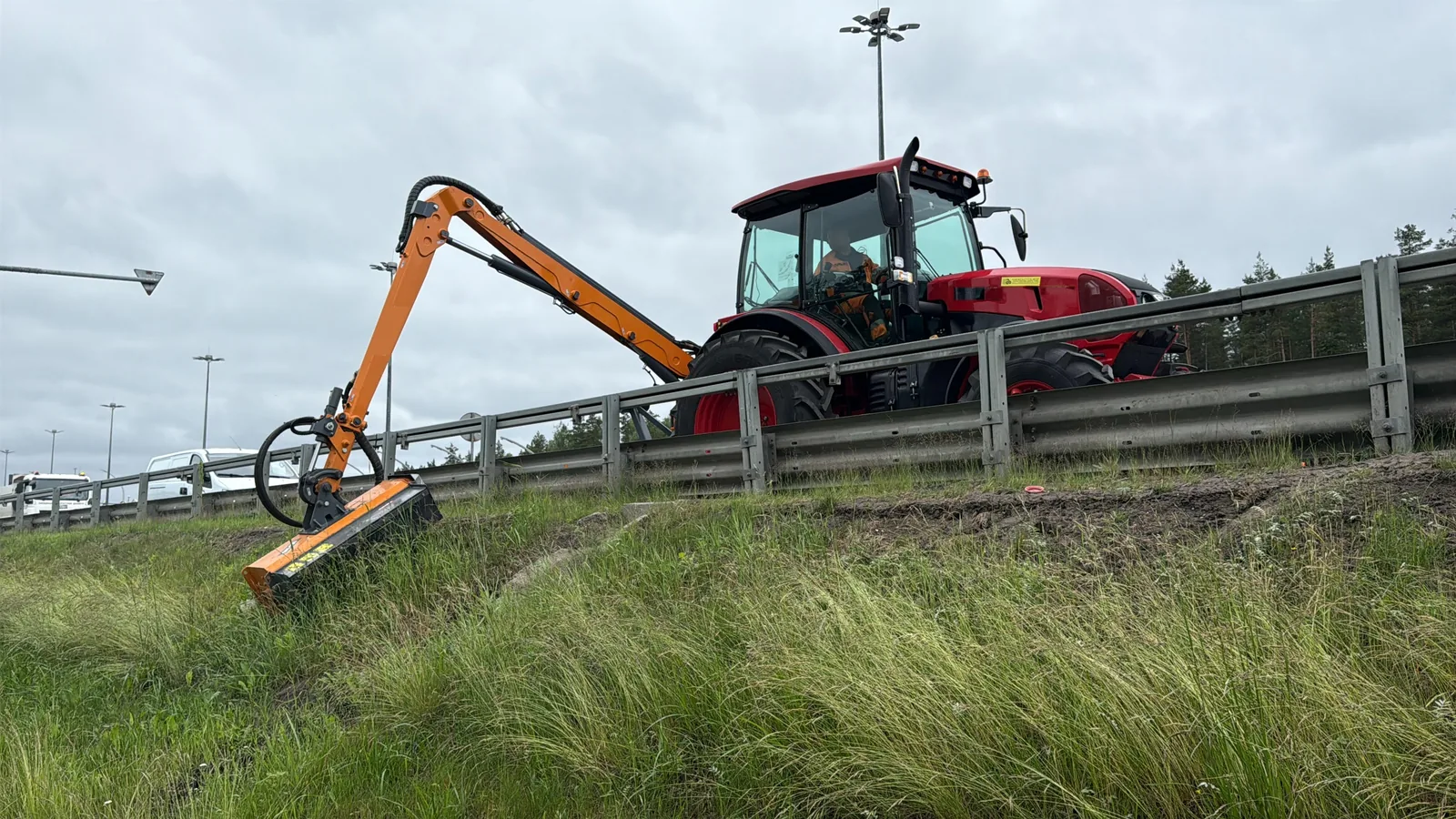 Ramenová sekačka Rolmex na traktoru — dlouhé hydraulické rameno s pracovní hlavou při sečení svahu u silnice